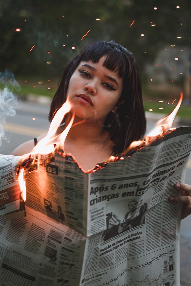 Chica sujetando un periódico ardiendo